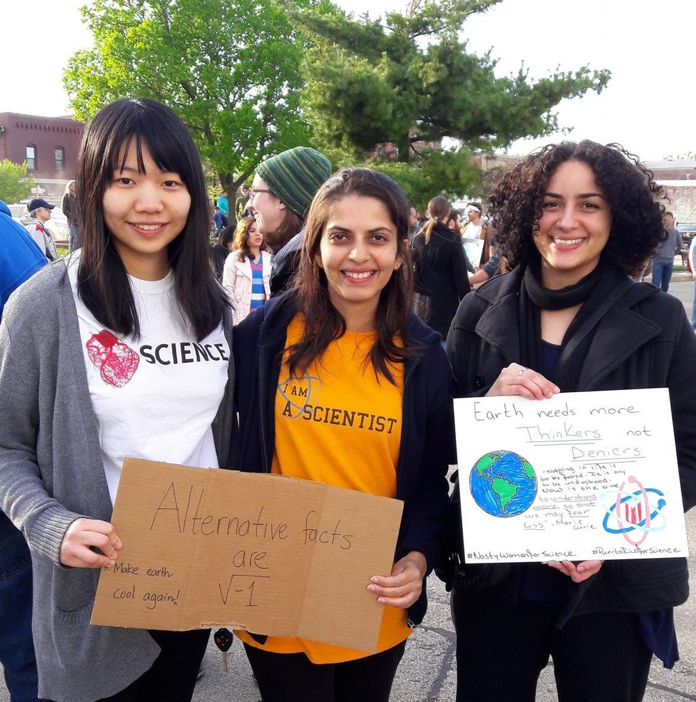 3 female graduate students holding their signs at the Champaign-Urbana March for Science