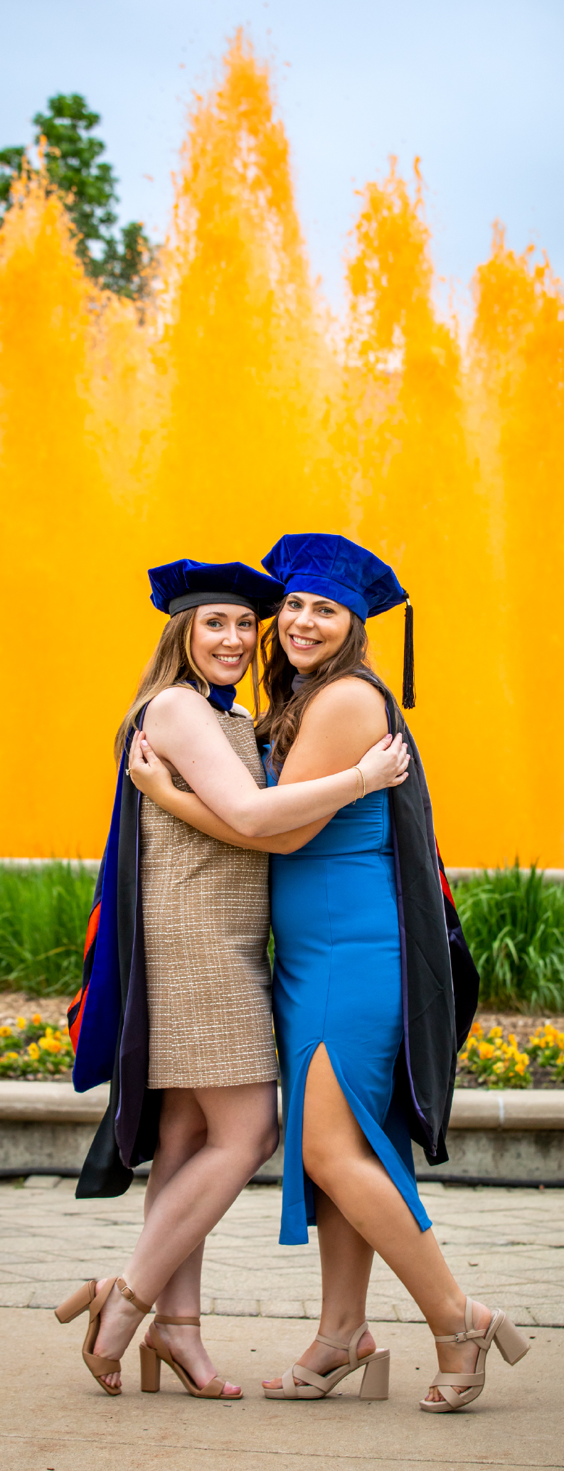 Two doctoral graduates hugging infront of the orange dyed fountain